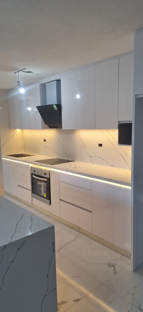 Cocina en blanco alto brillo con salpicadero y tope de cuarzo en cascada Calacatta y tiras LED