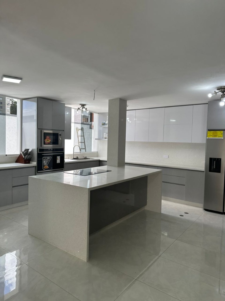 Cocina empotrada amplia con isla central gris y acabados en blanco brillante